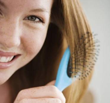Woman smiling holding a hairbrush and considering non-surgical hair restoration