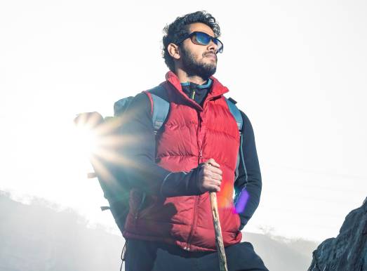 Man hiking in the mountains with sunglasses, warm clothes, a walking stick, and a full beard after having a natural hair transplant