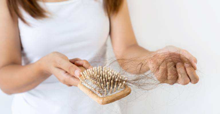 Woman wearing white, holding a brush with lots of hair after experiencing postpartum hair loss