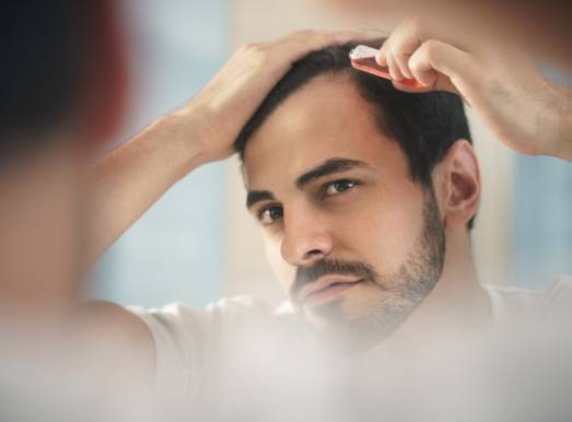 Attractive man with a beard and dark brown hair Repairing his Damaged Hair while grooming himself