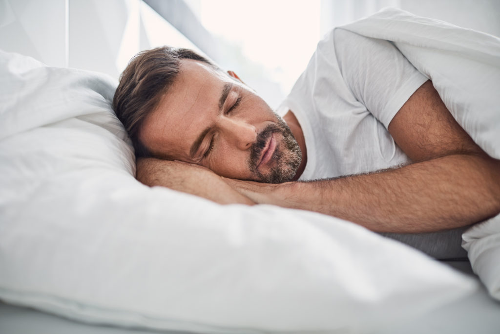 A middle-aged man with brown hair and a light beard sleeping peacefully after having a Hair Transplant